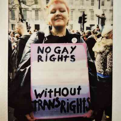 A person holds a colorful sign reading "No gay rights without trans rights" at a protest.