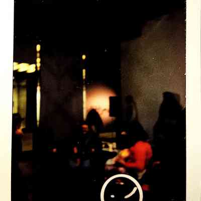 A dark lit polaroid which vaguely shows tables with people around them.