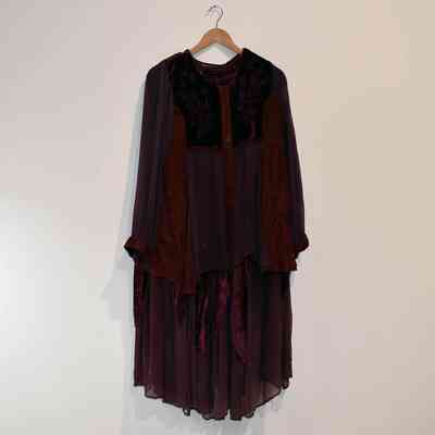 A long-sleeved, dark purple dress hangs on a wooden hanger against a plain, white wall.