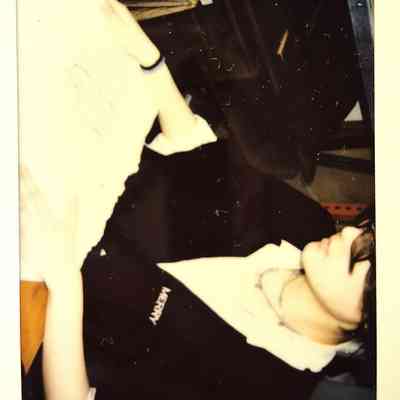 A person sits at a table, looking at something off-frame, wearing a dark apron.