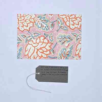 The image shows a floral pattern on pink, accompanied by a handwritten note on a tag.