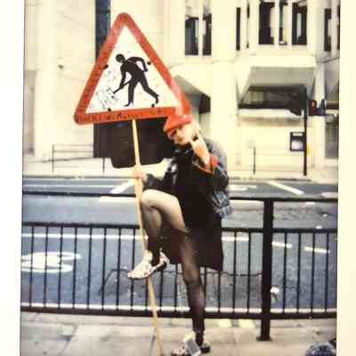 A person poses with a protest sign, wearing a red hat.