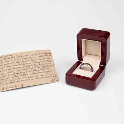 Dark red box with soft grey lining. Inside is a metal ring with a wood circle along the middle of the outside edge.