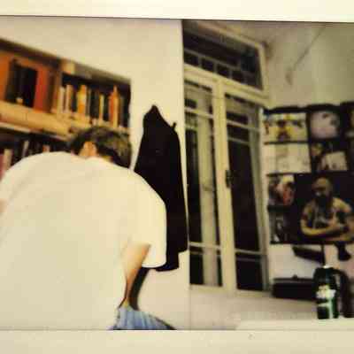 A person in a white shirt is sitting, facing shelves filled with books near a window.