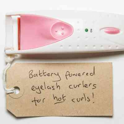 Handheld battery operated eyelash curler. It is white with pink buttons and the brand "citychick" written in black on the bottom of the handle.