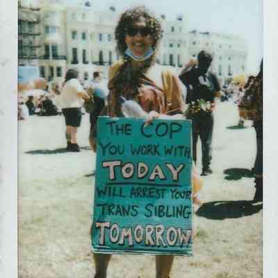 A person holds a sign saying, "The cop you work with today will arrest your trans sibling tomorrow".