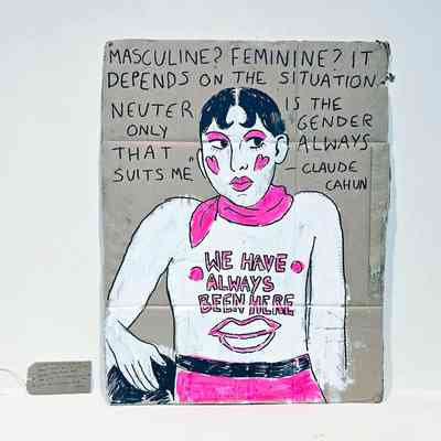 A brown cardboard placard painted with the image of a topless person with black hair, a pink scarf and pink trousers. The text "WE HAVE ALWAYS BEEN HERE" is written o n their chest. Above the painting is a quote about gender expression from Claude Cahun. With a brown, handwritten luggage tag.