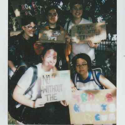 A group of five people are holding colorful signs advocating for trans rights and environmental issues.