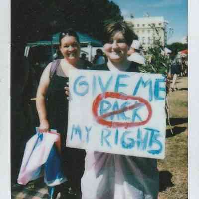 Two people stand together, one holding a sign that reads "Give Me My Rights."