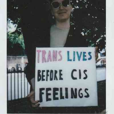 A person holds a sign reading "Trans Lives Before Cis Feelings" with "TP London 24" written at the bottom of the polaroid.