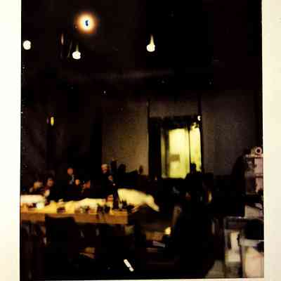 A dark lit polaroid which vaguely shows tables with people around them.