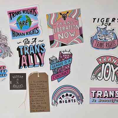 The image features colorful stickers advocating for transgender rights with supportive messages and imagery.