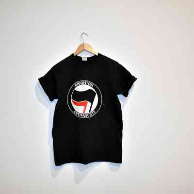 A black t-shirt with the "Brighton Antifascists" logo hangs on a wooden hanger.