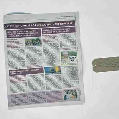 A copy of the Erdinton Local newspaper. It is opened at page 11 and shows an article on Homelessness in the Queer Community written by the donor. With a brown, handwritten luggage tag.