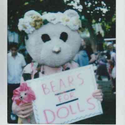 A person in a bear costume holds a sign reading "Bears for Dolls".