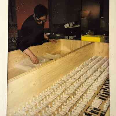 A person stands by a wooden box, preparing numerous small white objects in neat rows inside.