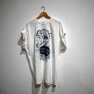 A white T-shirt with an artistic design hangs against a plain wall background.