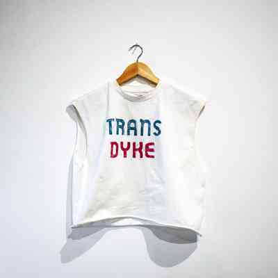 A white sleeveless shirt hangs on a wooden hanger, with Trans Dyke on it.