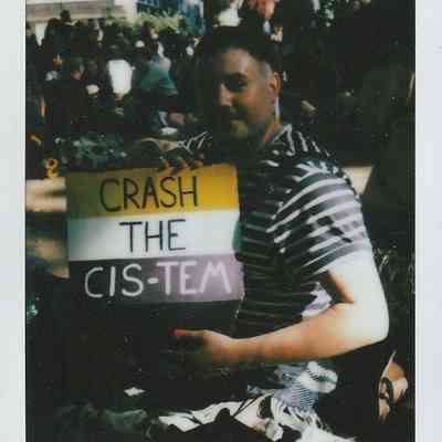 A person is holding a colorful sign that reads "CRASH THE CIS-TEM".