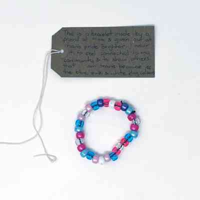 A bead bracelet made from blue, pink, white and clear beads. With a brown, handwritten luggage tag.