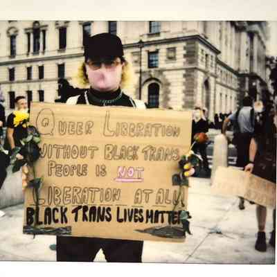 A person in a crowd holds a sign advocating for Black trans lives and queer liberation at a protest.