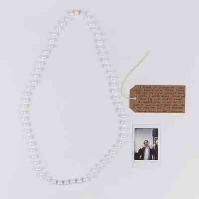 A pearl necklace, brown tag with writing on it and a polaroid of someone holding up the pearl necklace.