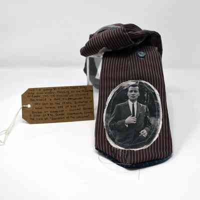 A brown, pinstripe tie featuring a picture of Stormé DeLarverié. With a brown, handwritten luggage tag.