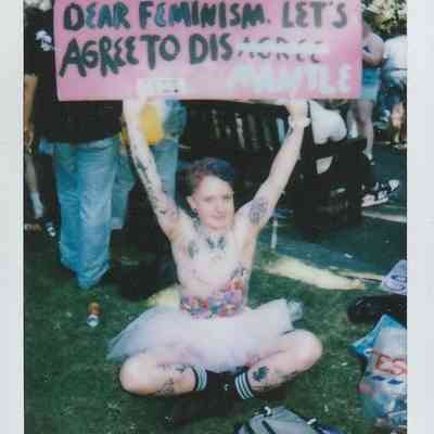 A person in a tutu holds a sign reading, "Dear feminism, let's agree to disMANTLE".