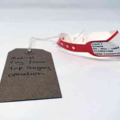 A medical tag labeled "Top Surgery Operation" rests beside a white and red hospital bracelet.