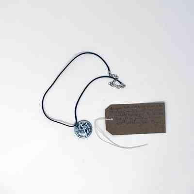 A necklace with a circular pendant lies beside a brown tag with handwritten text.
