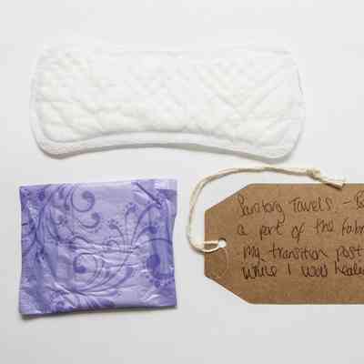 One white sanitary pad is laid lengthwise across the top of the photo. Directly underneath is a folded/ still packaged pad in light purple wrapping.