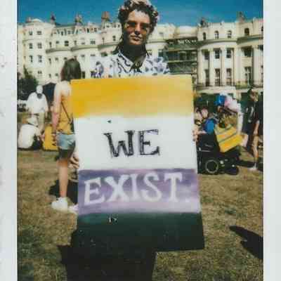 A person proudly holds a sign reading “We Exist” at a Trans Pride event in Brighton.