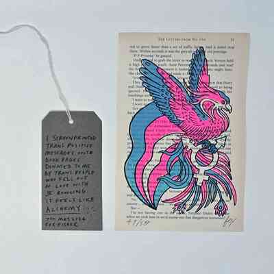 A page from a Harry Potter book shows a colorful phoenix drawing in trans flag colours with a tag describing the artwork’s trans-positive message.