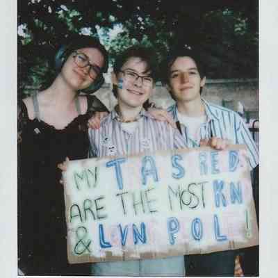 Three people stand together, smiling, holding a colorful sign with supportive text written on it.