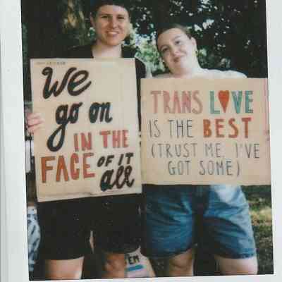 Two people are holding signs with supportive messages, standing together in an outdoor setting.