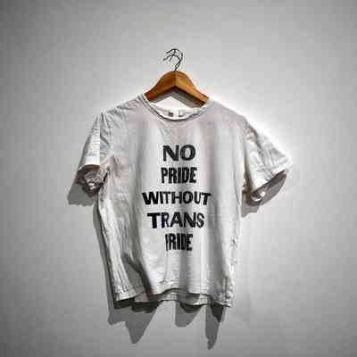 A white T-shirt on a hanger displays the message: "No pride without trans pride."