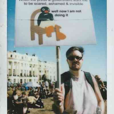 A person stands holding a protest sign which says "When the press & government want me to be scared, ashamed & visible" with an image of Pingu the penguin sat on a chair which then reads "well now I am not doing it".