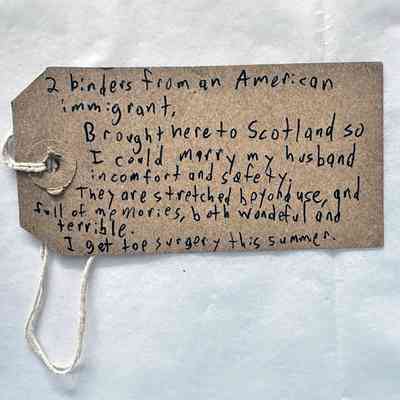 A handwritten note on a brown tag shares a personal narrative about binders and top surgery.
