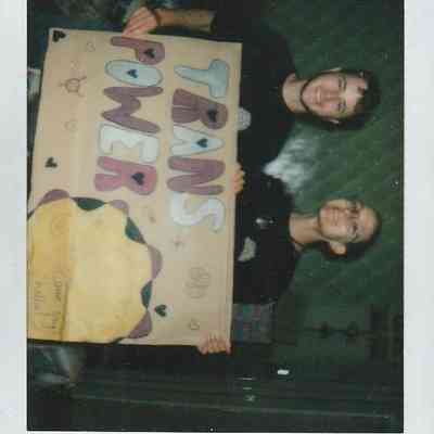 Two people happily hold a colorful "Trans Power" sign at the Trans Pride event in Brighton.