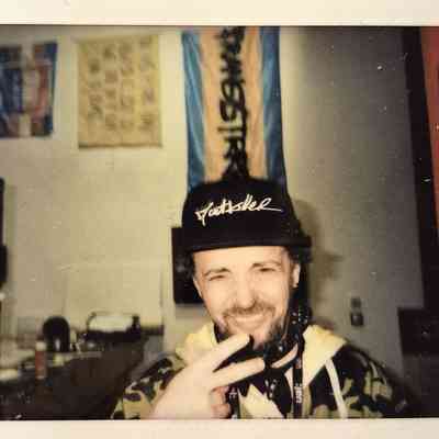 A smiling person wearing a cap flashes a peace sign while posing indoors with flags behind them.