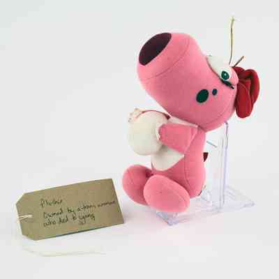 A pink plushie toy of Birdo holding a ball. With a brown, handwritten luggage tag.