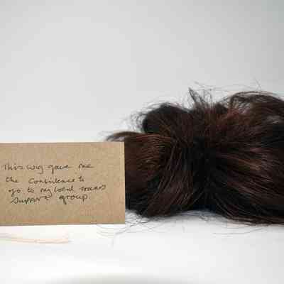 A dark brown wig with a brown handwritten luggage tag.
