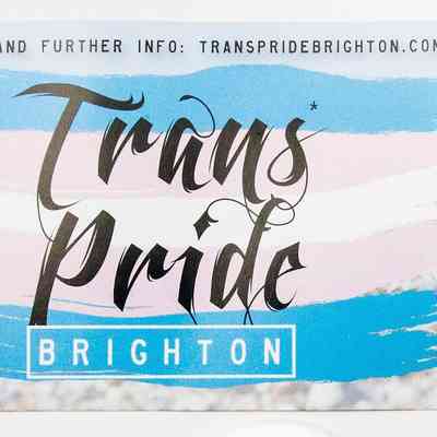 Flyer; front has flag shape pink, blue, white reads "Trans*pride Brighton July 25th, 26th & 27th" Reverse; photo of beach pebbles & sky, info on events July 2014.