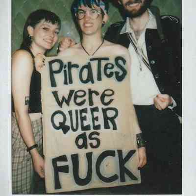 Three people pose for a photo, holding a bold sign about pirates.