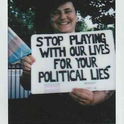 A person holds a sign saying, "STOP PLAYING WITH OUR LIVES FOR YOUR POLITICAL LIES".