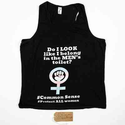 A black vest top depicting the feminist resistance symbol in the trans colours, stylised with a raised fist and the text "Do I LOOK like I belong in the MEN's toilet" "#CommonSense""#ProtectALLwomen". Also, a brown, handwritten luggage tag.