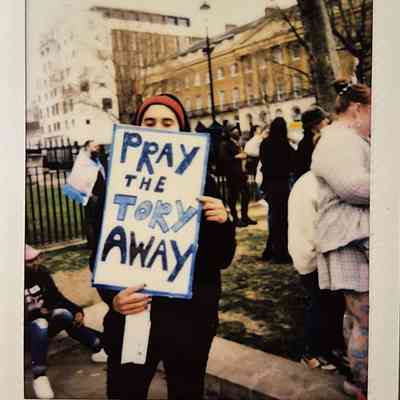 A person holds a sign reading "Pray the Tory Away" at a public protest gathering in London.