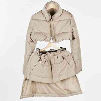 A beige, quilted jacket and matching skirt are hanging on a wooden hanger.