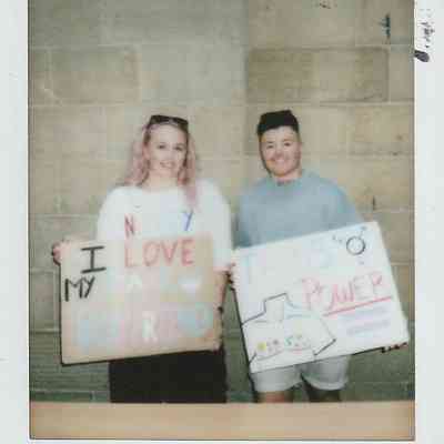 Two people smiling while holding colorful signs at an event.