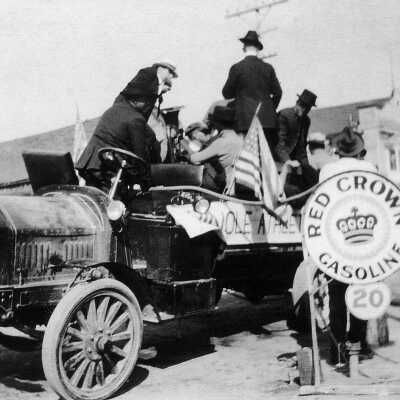 Stopping for gasoline in vintage auto with seven unidentified individuals.